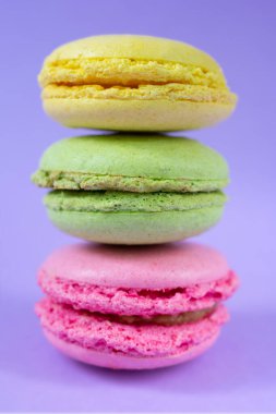 Üçlü Fransız renkli kurabiyeler mor arka planda üst üste. Farklı dahili katmanlı dikey bisküvi yığını kapat