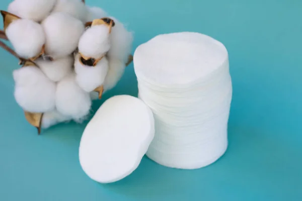 Group of white cosmetic pads on blue background with cotton flowers. Hypoallergenic recyclable ccessories for removing make up.