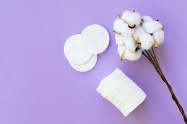 Menekşe arkaplan üzerinde açık pamuk çiçekleriyle beyaz pamuk pedlerin üst görüntüsü. Makyajı kaldırmak için aksesuarlar. Hipoalerjenik ve geri dönüştürülebilir.