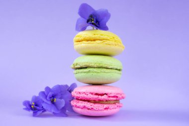 Dikey badem kurabiyeleri üst üste dizilmiş. Mor Afrika menekşeleriyle süslenmiş renkli badem bisküvileri..