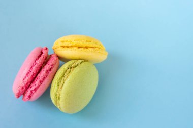 Mavi arka planda üç renkli badem kurabiyesi ve fotokopi alanı. Pembe, sarı ve yeşil Fransız geleneksel bademli kurabiyeleri.