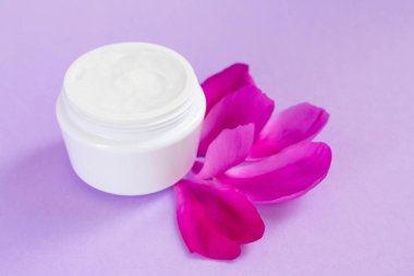 Şakayık özlü beyaz nemlendirici krem ve pembe arka planda taç yaprakları.