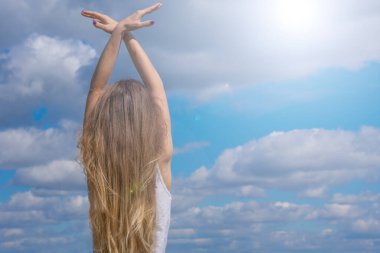 Sarı saçlı kadın arkada duruyor. Mavi bulutlu arka plan ve parlak güneş ışığı üzerinde kuş hareketleriyle ellerini kaldırmış genç bir kadın. Özgürlük, fırsatlar ve sakinlik metaforu.