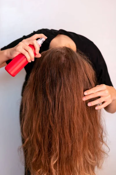 Young woman spraying her wavy blond long hair for sun and heat protection. Treatment for hair loss and strength.