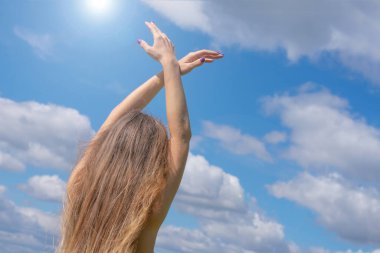 Güneşli, genç, sarışın bir kadın. Mavi bulutlu arka plan ve parlak güneş ışığı üzerinde kuş hareketleriyle ellerini kaldırmış duruyor. Aşk havası, özgürlük ve sakinlik kavramı.