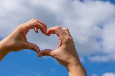 Genç kadın kalp şeklinde el hareketi ile parlak mavi gökyüzü doğal arka planında. Uzayı kopyala Metafor ya da aşk havası, sükunet ve aile ilişkisi kavramı. Parlak yaz güneşi