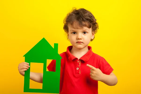 The boy points his finger at the green layout of the house. The child in the red shirt shows the finger that you need to stay at home. On a yellow background