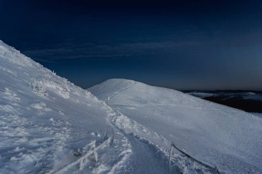Soğuk bir kış günü Bieszczady Dağları 'nda karla kaplı Poonina Caryska. Açık dağ sırtı, donmuş patika, dramatik bulutlar ve açık gökyüzü Polonya dağlarında klasik bir kış yürüyüşü manzarası yaratır..
