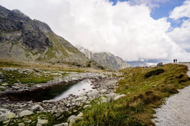 Yüksek dağ gölü Velk Hincovo pleso, Slovakya 'nın başkenti High Tatras' ta kayalık tepeler ve dramatik bulutlarla çevrilidir. Uzak dağlık arazi ve vahşi doğa manzarası.