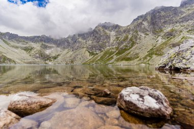 Yüksek dağ gölü Velk Hincovo pleso, Slovakya 'nın başkenti High Tatras' ta kayalık tepeler ve dramatik bulutlarla çevrilidir. Uzak dağlık arazi ve vahşi doğa manzarası.