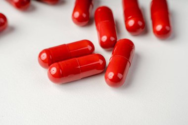 Beyaz arka planda açık bir şişeden saçılan kırmızı kapsüller, ilaveleri, ilaçları, enerji haplarını ve modern sağlık hizmetleri kavramlarını sembolize ediyor..