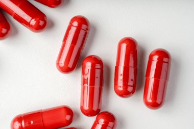 Beyaz arka planda açık bir şişeden saçılan kırmızı kapsüller, ilaveleri, ilaçları, enerji haplarını ve modern sağlık hizmetleri kavramlarını sembolize ediyor..