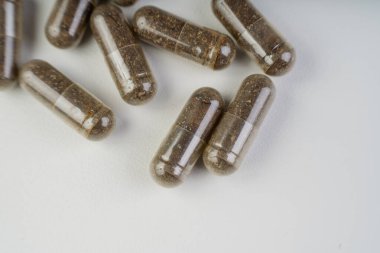 Kahverengi bitkisel kapsüllerin yakın plan resmi beyaz arka planda cam bir şişeden döküldü. Doğal destek kavramı, sağlık, alternatif tıp ve temiz kopya alanı ile beslenme desteği.