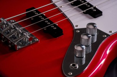 Telleri, köprüyü ve pikapları gösteren dört telli kırmızı bir bas gitarın yakın plan detayları. Müzik aleti arkaplanı.