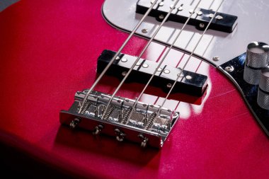 Telleri, köprüyü ve pikapları gösteren dört telli kırmızı bir bas gitarın yakın plan detayları. Müzik aleti arkaplanı.