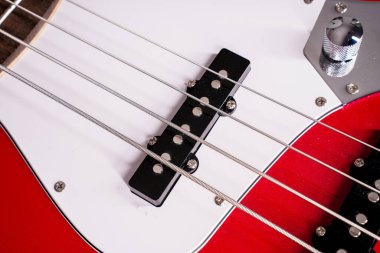 Telleri, köprüyü ve pikapları gösteren dört telli kırmızı bir bas gitarın yakın plan detayları. Müzik aleti arkaplanı.