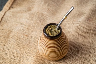 Yerba mate metal bombilla ile seramik bir materyalde hizmet verdi, sade bir yaşam kompozisyonu içinde rustik çuval bezi kumaşında fotoğraflandı.