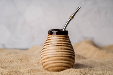 Yerba mate metal bombilla ile seramik bir materyalde hizmet verdi, sade bir yaşam kompozisyonu içinde rustik çuval bezi kumaşında fotoğraflandı.