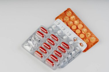 Beyaz arka planda düzenlenmiş tablet ve kırmızı kapsüller içeren farklı kabarcık paketleri, temiz bir tıbbi durağan kompozisyonda fotoğraflanmıştır..