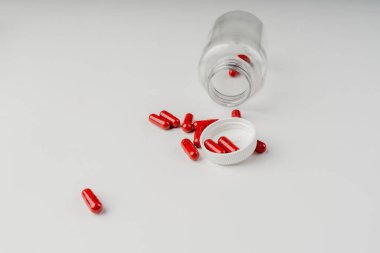 Kırmızı kapsüller beyaz arka planda açık plastik bir kutudan dökülmüş. Temiz bir tıbbi hayat olarak fotoğraflanmış..