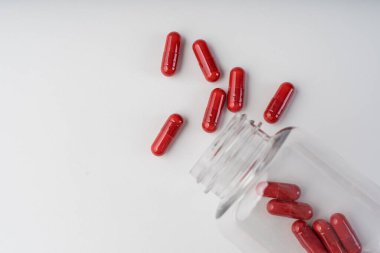 Kırmızı kapsüller beyaz arka planda açık plastik bir kutudan dökülmüş. Temiz bir tıbbi hayat olarak fotoğraflanmış..