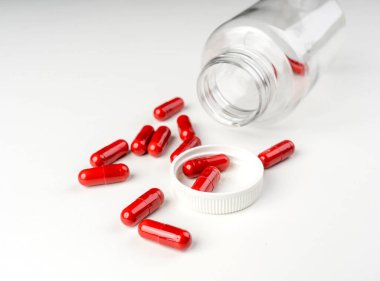 Kırmızı kapsüller beyaz arka planda açık plastik bir kutudan dökülmüş. Temiz bir tıbbi hayat olarak fotoğraflanmış..