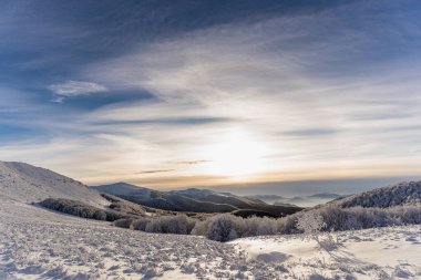 Mavi gökyüzü, altın saat ışığı ve panoramik dağ manzarası ile soğuk bir kış sabahı Bieszczady 'de kar yamaçlarını kapladı..