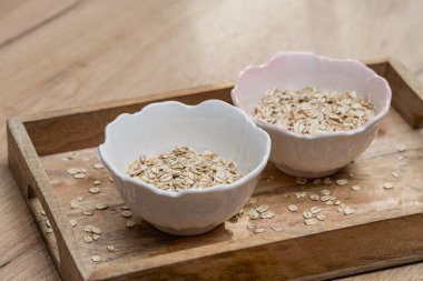 Çiğ yulaf gevrekleri küçük seramik kaselerde sunuluyor. Tahta tepside, doğal gıdayı, karbonhidratı ve sağlıklı bir diyet konseptini temsil ediyor..