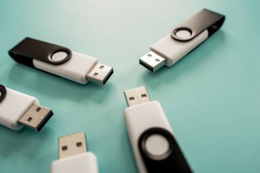 Portatif veri depolama ve dijital teknolojiyi temsil eden turkuaz bir yüzeye yerleştirilmiş çoklu siyah beyaz USB flash diskler.