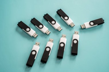 Portatif veri depolama ve dijital teknolojiyi temsil eden turkuaz bir yüzeye yerleştirilmiş çoklu siyah beyaz USB flash diskler.
