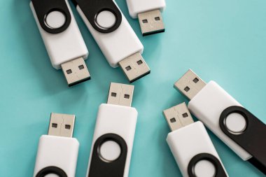Portatif veri depolama ve dijital teknolojiyi temsil eden turkuaz bir yüzeye yerleştirilmiş çoklu siyah beyaz USB flash diskler.
