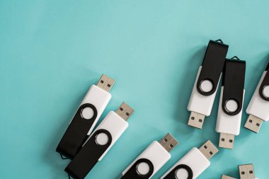Portatif veri depolama ve dijital teknolojiyi temsil eden turkuaz bir yüzeye yerleştirilmiş çoklu siyah beyaz USB flash diskler.