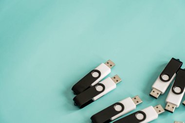 Portatif veri depolama ve dijital teknolojiyi temsil eden turkuaz bir yüzeye yerleştirilmiş çoklu siyah beyaz USB flash diskler.