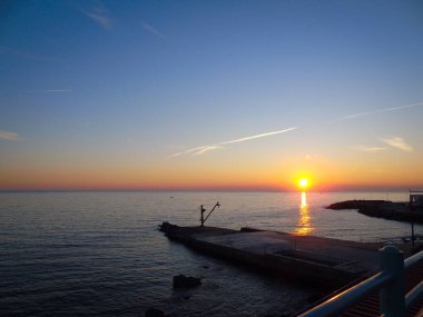 Cenova, İtalya - 26 Şubat 2021: Cenova Denizi üzerinde kış günleri güzel bir günbatımı. İnanılmaz kırmızı ve turuncu renkli gökyüzü suya yansıyor..