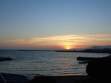 Cenova, İtalya - 10 Mart 2021: Cenova Denizi üzerinde kış günleri güzel bir günbatımı. İnanılmaz kırmızı ve turuncu renkli gökyüzü suya yansıyor..