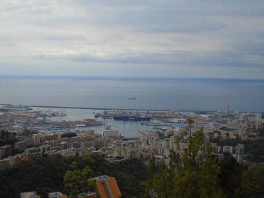 Cenova, İtalya - 14 Nisan 2021: Genova şehri üzerindeki dağlara ve limanın küçük bir kısmına panoramik manzara. Arka planda gri gökyüzü.