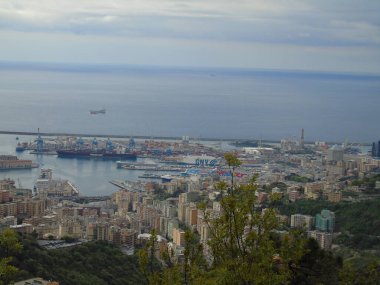 Cenova, İtalya - 14 Nisan 2021: Genova şehri üzerindeki dağlara ve limanın küçük bir kısmına panoramik manzara. Arka planda gri gökyüzü.