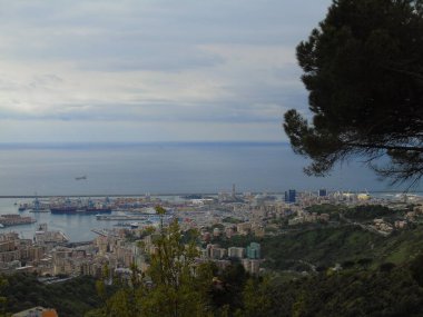 Cenova, İtalya - 14 Nisan 2021: Genova şehri üzerindeki dağlara ve limanın küçük bir kısmına panoramik manzara. Arka planda gri gökyüzü.