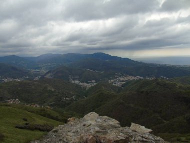 Cenova, İtalya - 14 Nisan 2021: Genova şehri üzerindeki dağlara ve limanın küçük bir kısmına panoramik manzara. Arka planda gri gökyüzü.