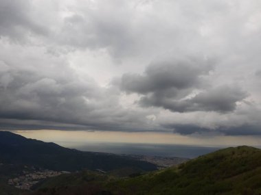 Cenova 'nın etrafındaki dağları keşfetmek. Şehrin panoramik manzarası. Arka planda gri gökyüzü. Baharın ilk yeşil yaprakları.