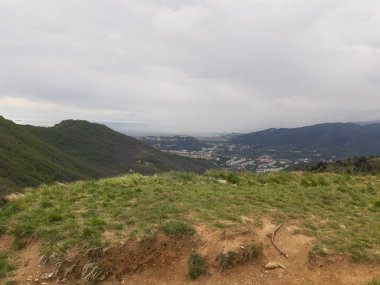 Cenova 'nın etrafındaki dağları keşfetmek. Şehrin panoramik manzarası. Arka planda gri gökyüzü. Baharın ilk yeşil yaprakları.