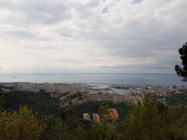 Cenova 'nın etrafındaki dağları keşfetmek. Şehrin panoramik manzarası. Arka planda gri gökyüzü. Baharın ilk yeşil yaprakları.