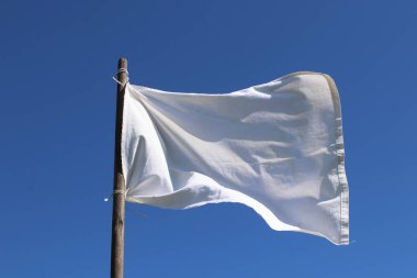 The white flag against the blue sky.  Surrender concept. clipart