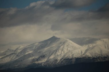 Bulutların üstünde kar ve güneş olan dağ seçimleri Mitsikeli Dağı 'nın arka planında kış buzları