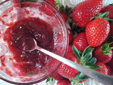 Çilekler. Kaşık kasesinde taze reçel. Meyve arka planında.