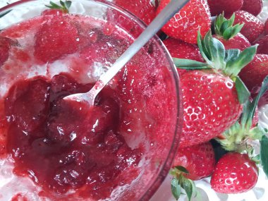 Çilekler. Kaşık kasesinde taze reçel. Meyve arka planında.