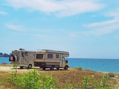 Yazın deniz kenarında bir karavan. Kumsal ağaçları. Mavi gökyüzü tatillerde seyahat ediyor.