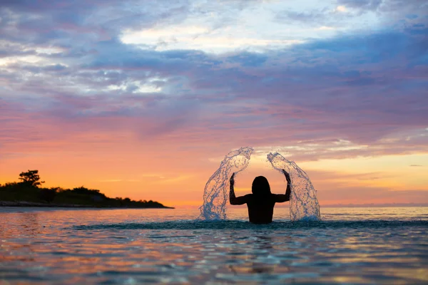 Man opspattend Water met zijn handen op een zee in een zonsopgang met co — Stockfoto