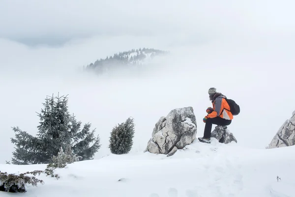 Zijaanzicht van een man in warme kleding rusten op een rots in de besneeuwde m — Stockfoto