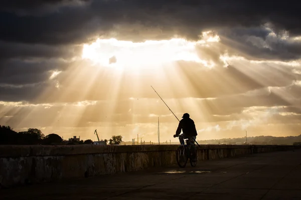 Silhueta de pescador na bicicleta com raios no fundo — Fotografia de Stock